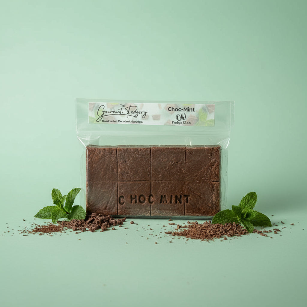 Choc mint fudge slab on a mint green background with mint leaves and chocolate shavings
