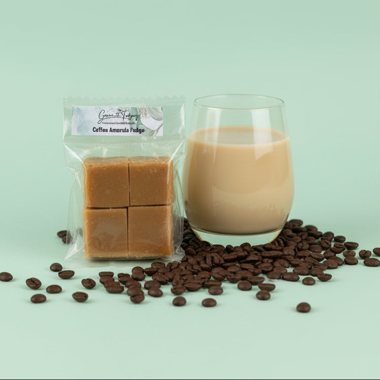 Two square coffee amarula fudge pieces in clear packaging on a mint green background with coffee beans and a glass of Amarula