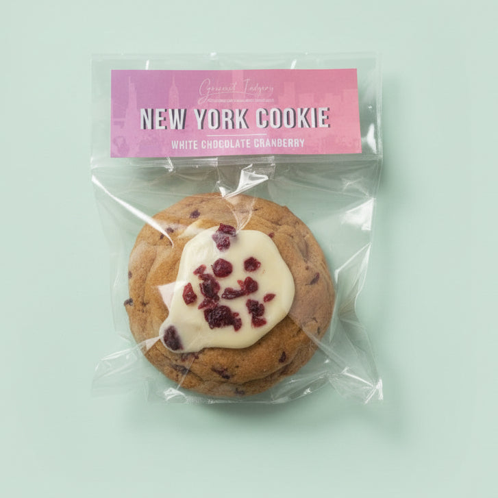 Cookie with white chocolate and cranberries in a clear package labeled 'New York Cookie' on a mint background